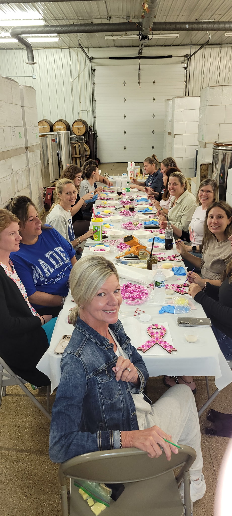 Guests seated along a long table, crafting pink ribbon mosaics in the winery
